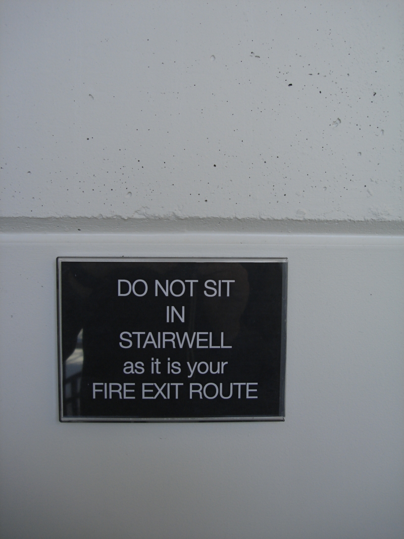 Sign telling people not to sit in the stairwell because it is a fire exit route.