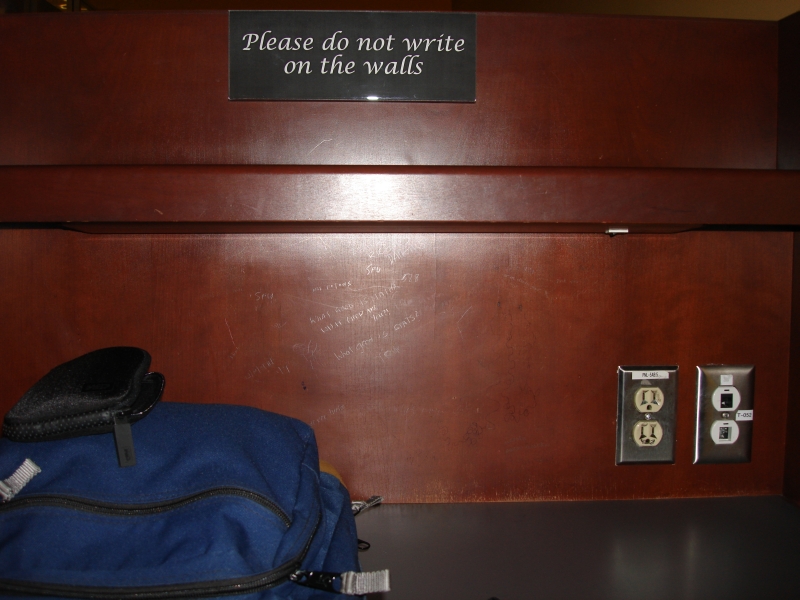 Back wall of a study carrel with writing on the well near a sign that says "Please do not write on the walls."